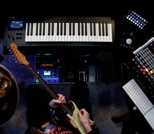 Kelly Richey playing electric guitar in her home studio with keyboard and music production equipment